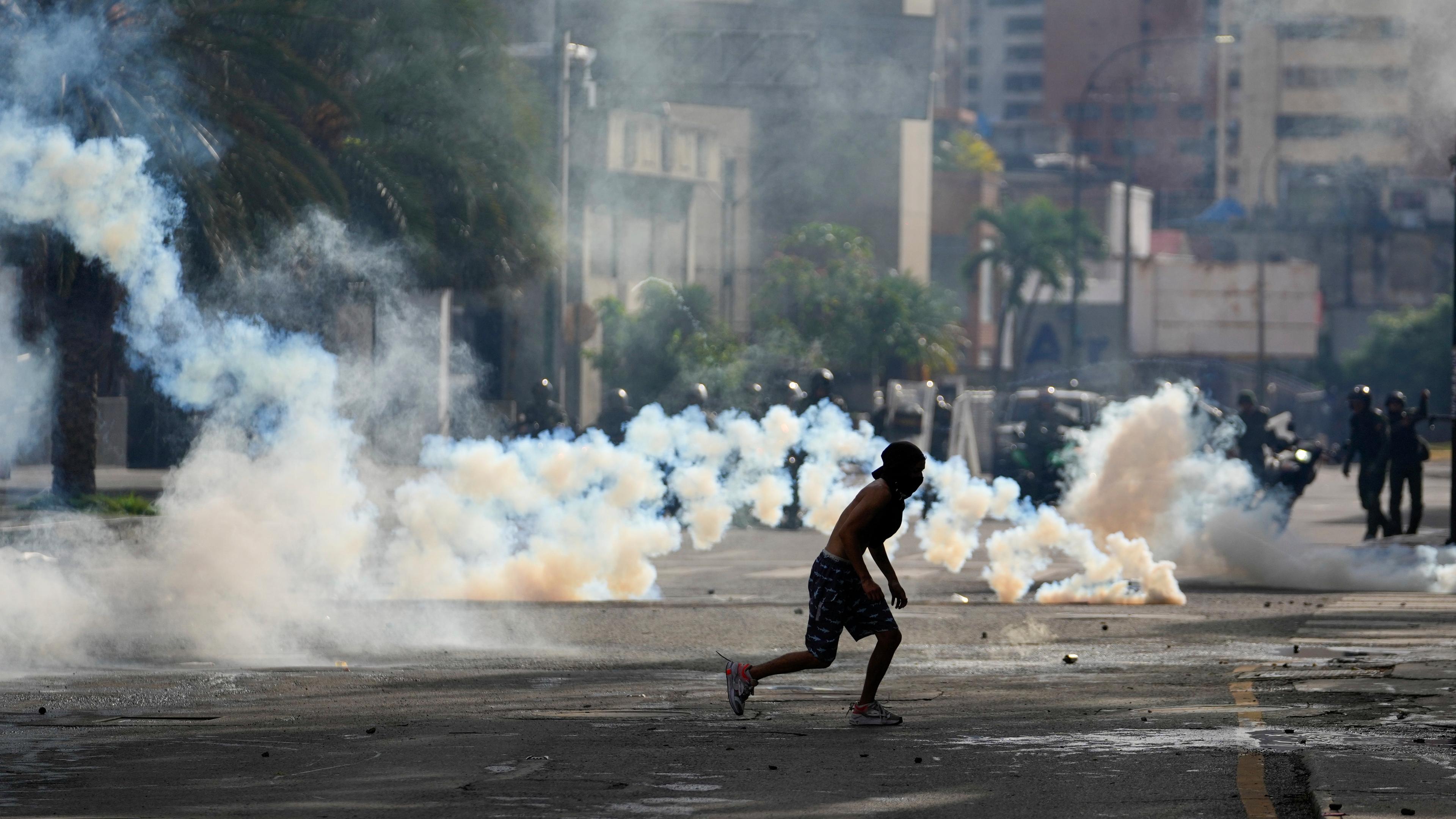 29.07.2024, Venezuela, Caracas: Ein Demonstrant rennt, während die Polizei bei Protesten gegen das offizielle Ergebnis der Präsidentenwahl Tränengas einsetzt.