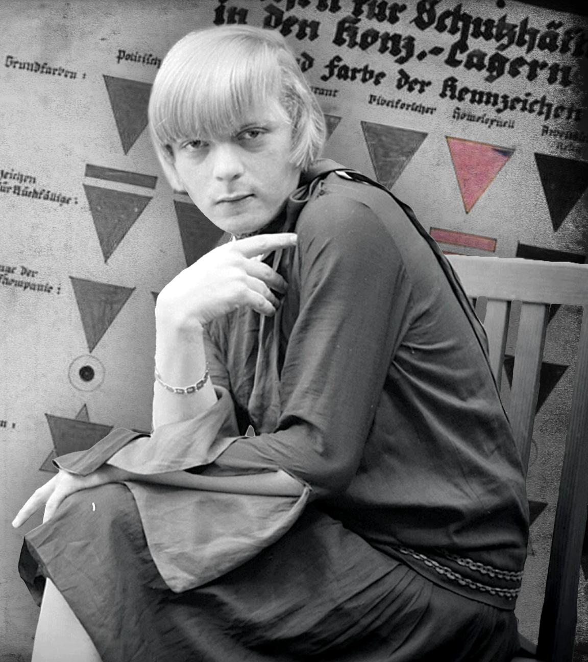 Transfrau Liddy Bacroff im Vordergrund. Im Hintergrund links Gefangene im Konzentrationslager Sachsenhausen; rechts eine Tafel mit KZ-Kennzeichen.