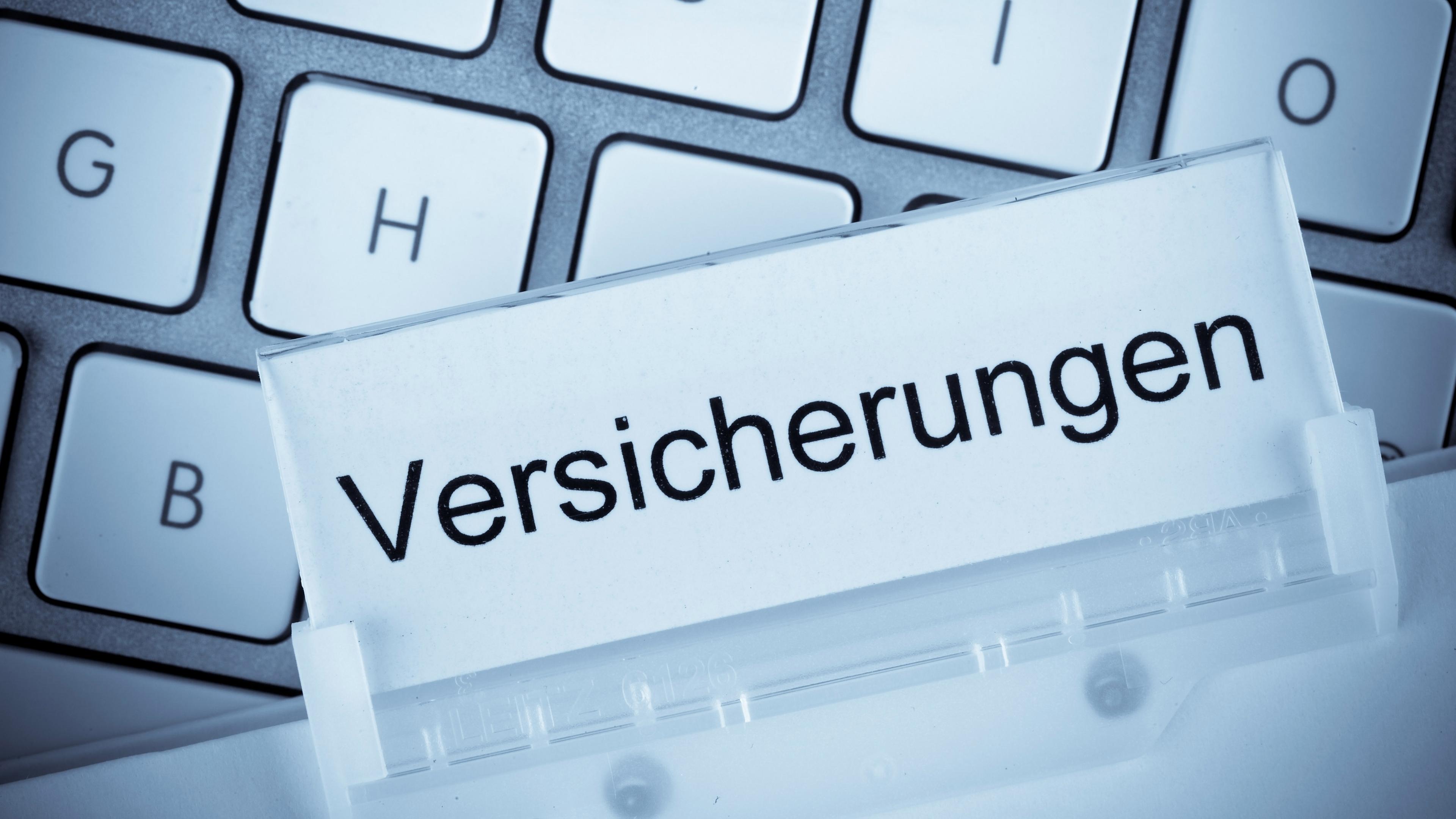 Eine Akte mit der Aufschrift "Versicherungen" auf einer Computertastatur.