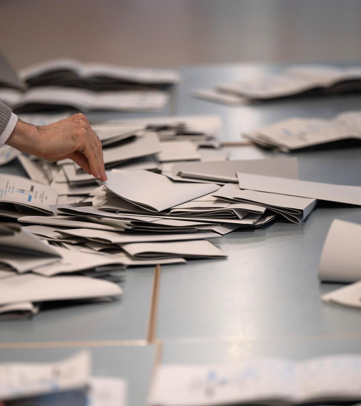 Wahlhelfer und Wahlhelferinnen zählen in einem Wahllokal Stimmzettel.