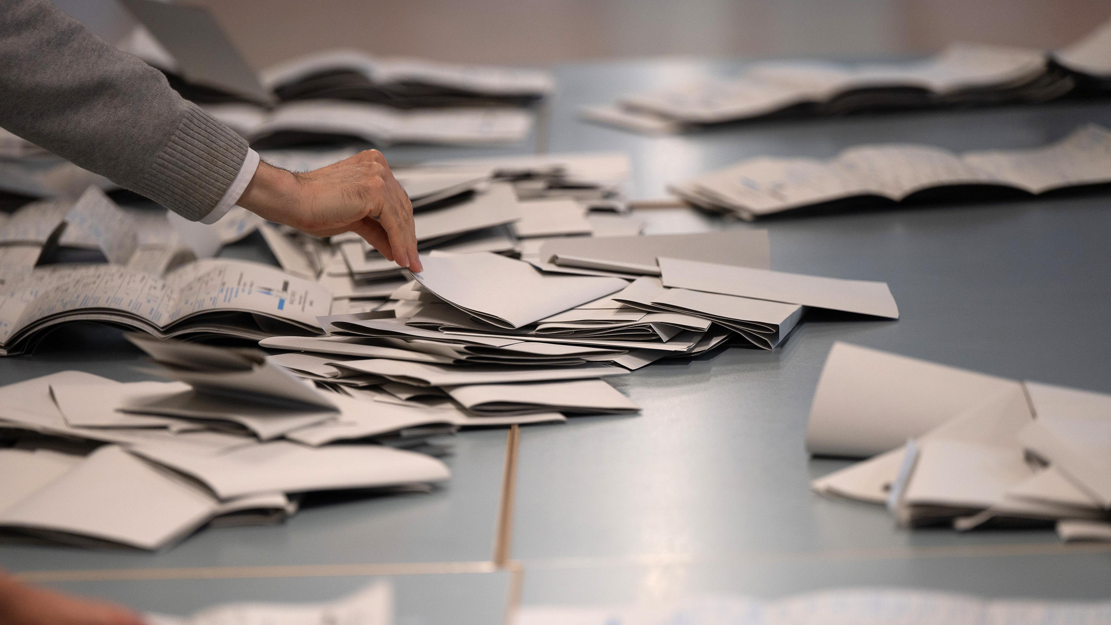 Wahlhelfer und Wahlhelferinnen zählen in einem Wahllokal Stimmzettel.