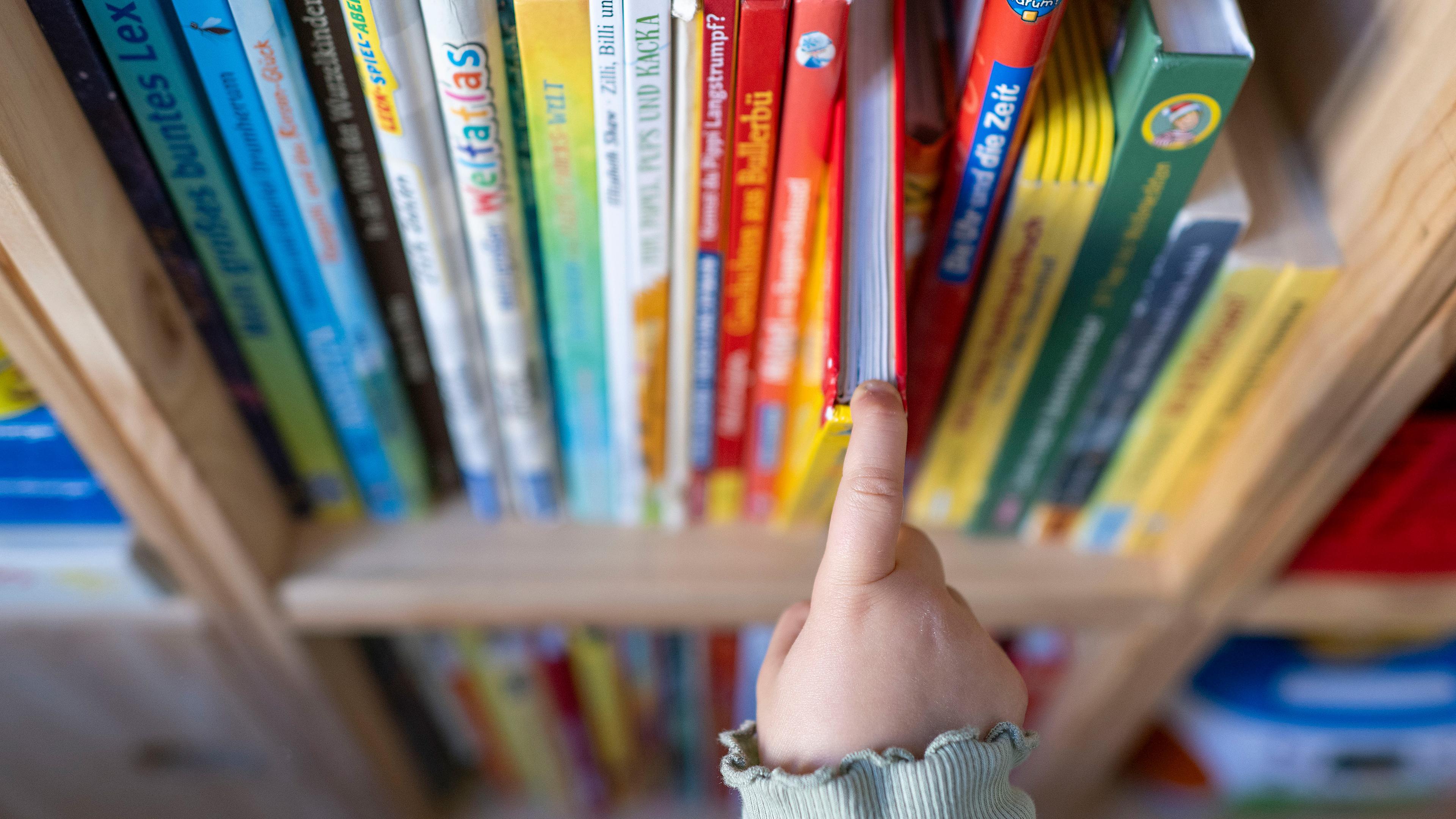 Ein Mädchen zieht in einem Kinderzimmer ein Kinderbuch aus einem Regal