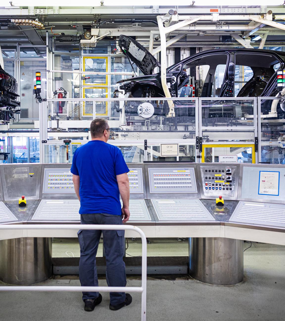 Ein Mitarbeiter überwacht im VW Werk an einem Schaltpult eine Fertigungsstrecke mit Autos.