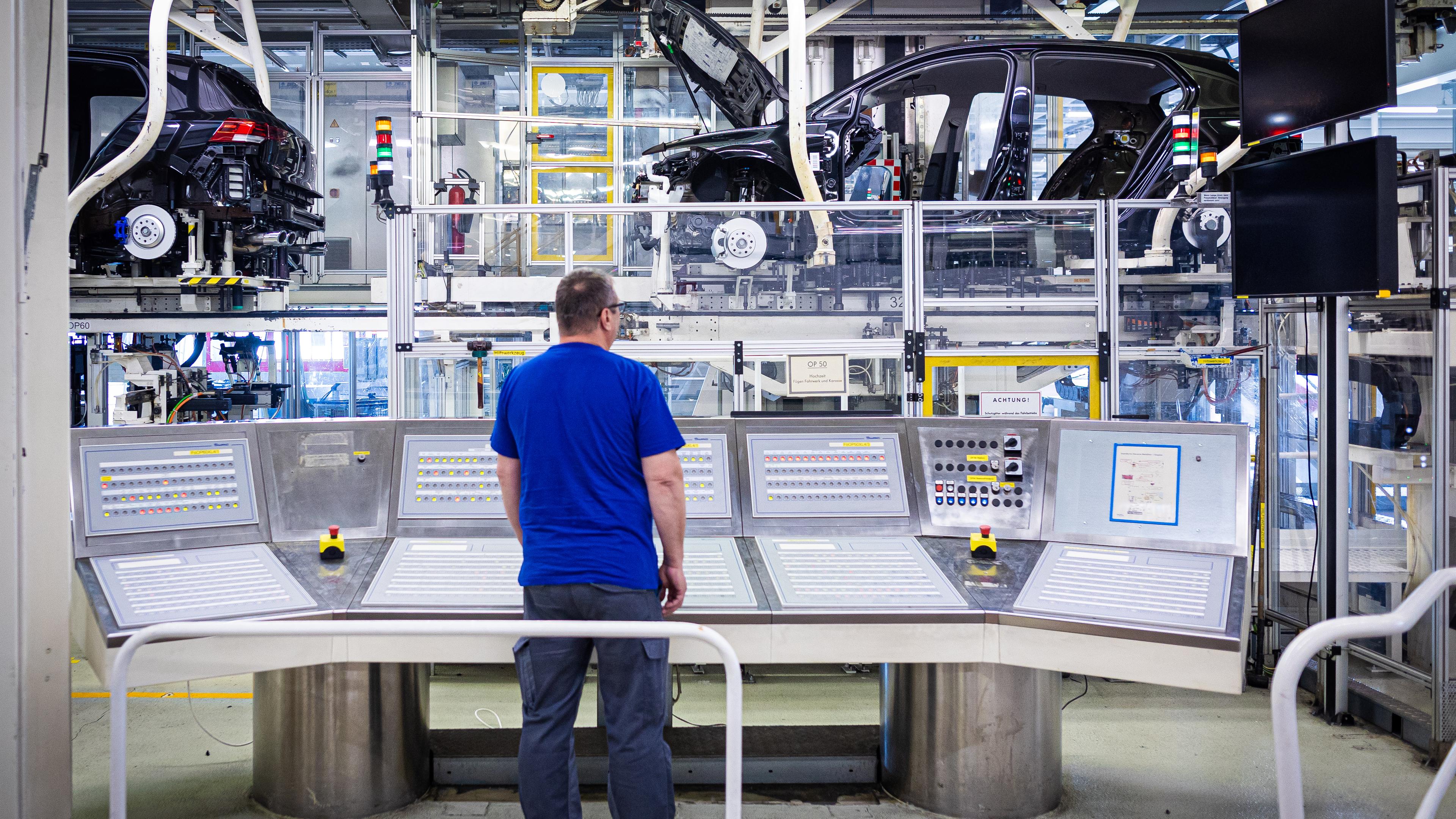 Ein Mitarbeiter überwacht im VW Werk an einem Schaltpult eine Fertigungsstrecke mit Autos.