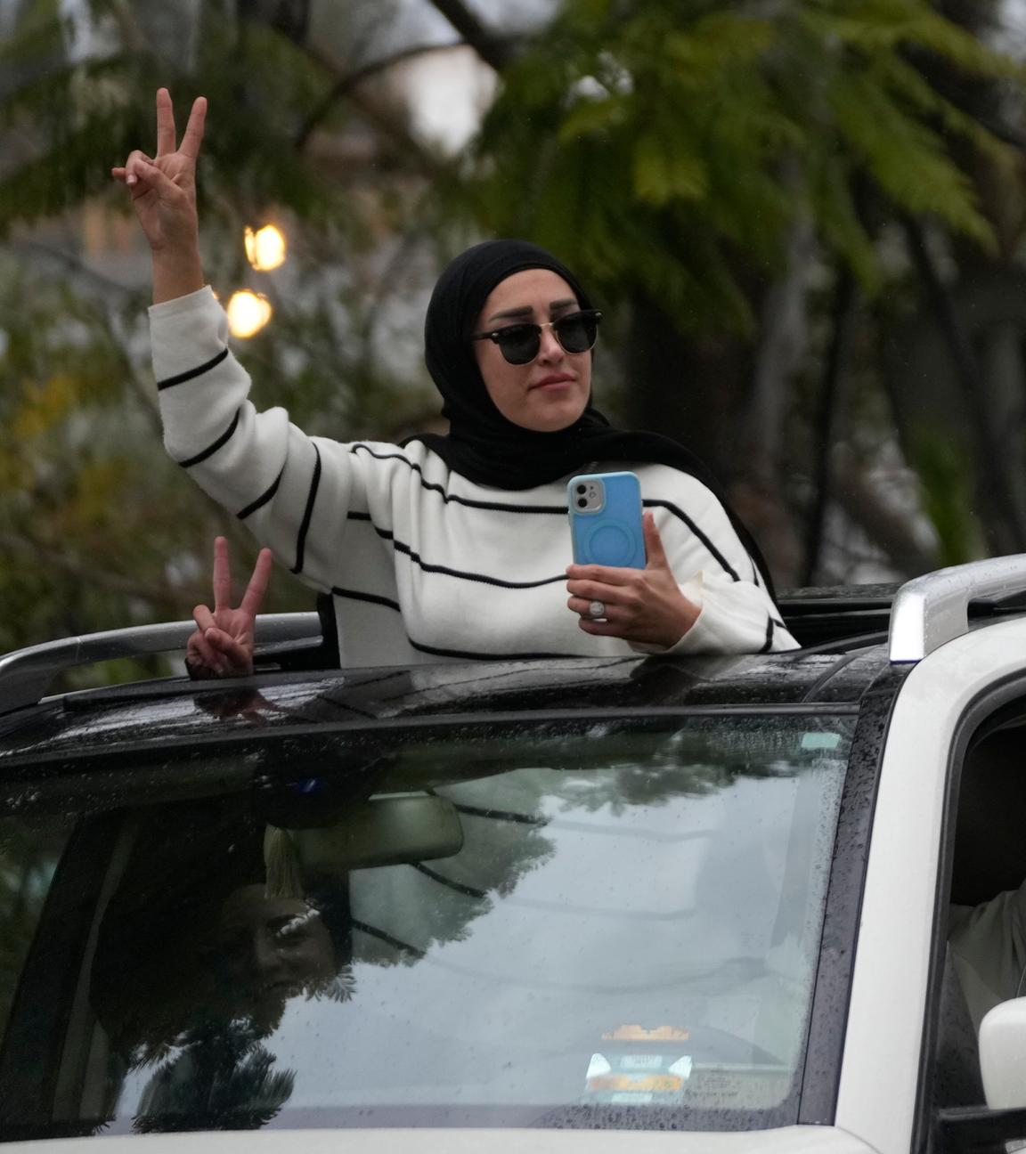 Frau schaut aus Autofenster und zeigt "Peace"-Zeichen.