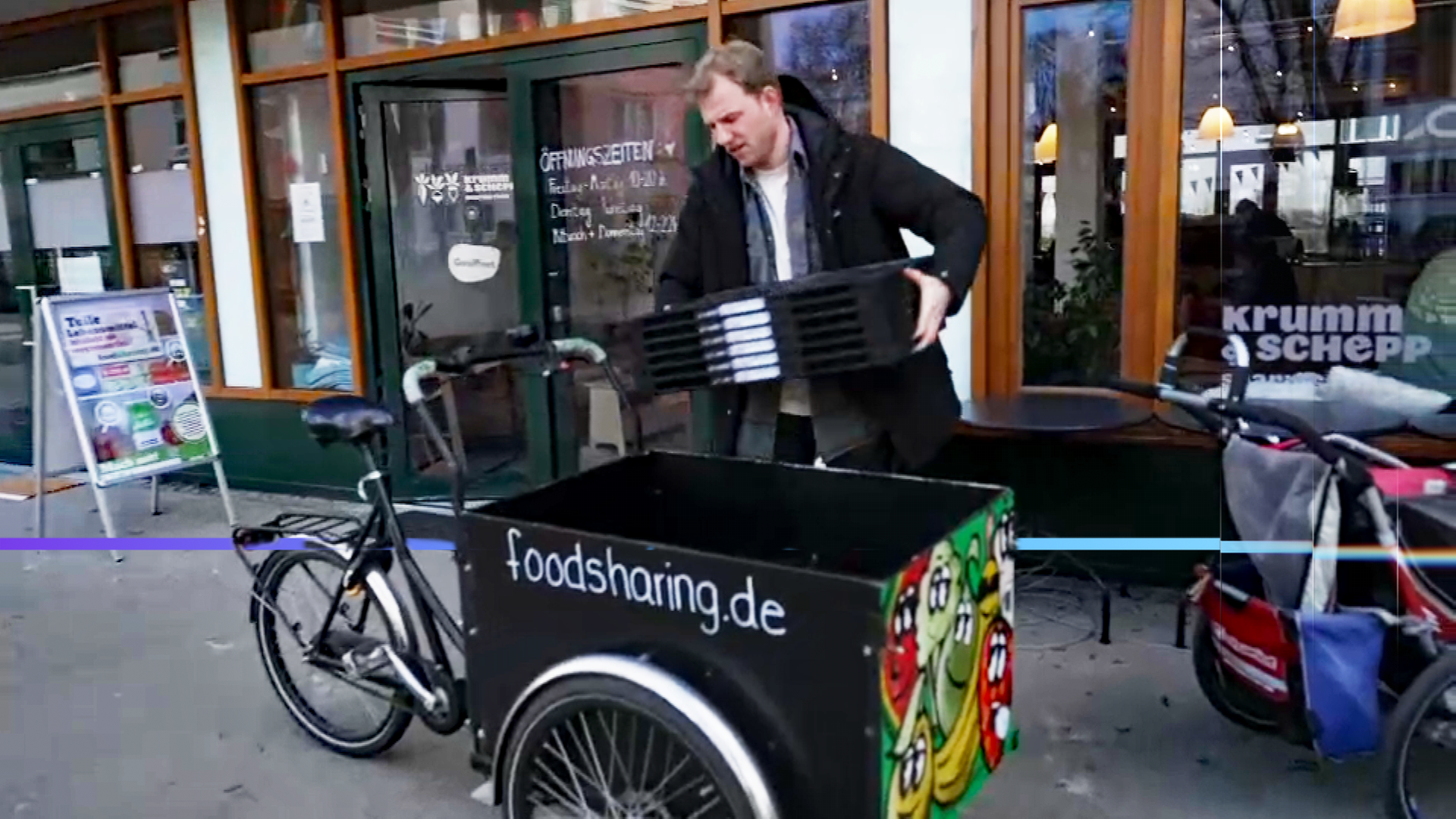 Ein Mann lädt auf einem Gehweg leere, zusammengeklappte Kisten in sein Lastenfahrrad. Auf dem Lastenfahrrad steht der Text "foodsharing.de". Im Hintergrund ist der Eingang zu einem Lebensmittelgeschäft zu sehen.