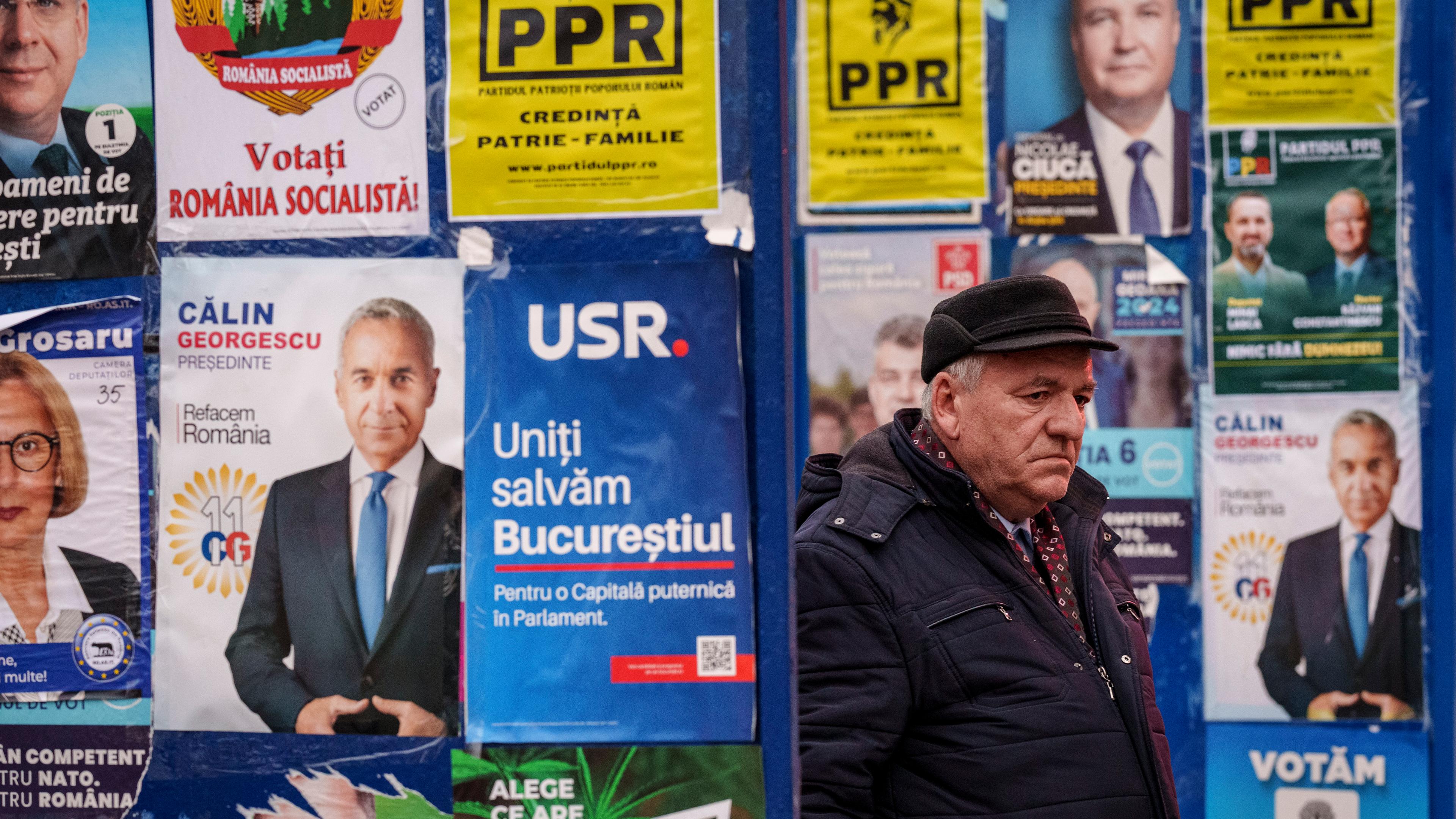 Ein Mann geht an einer Wand, die mit Wahlplakten beklebt ist vorbei.