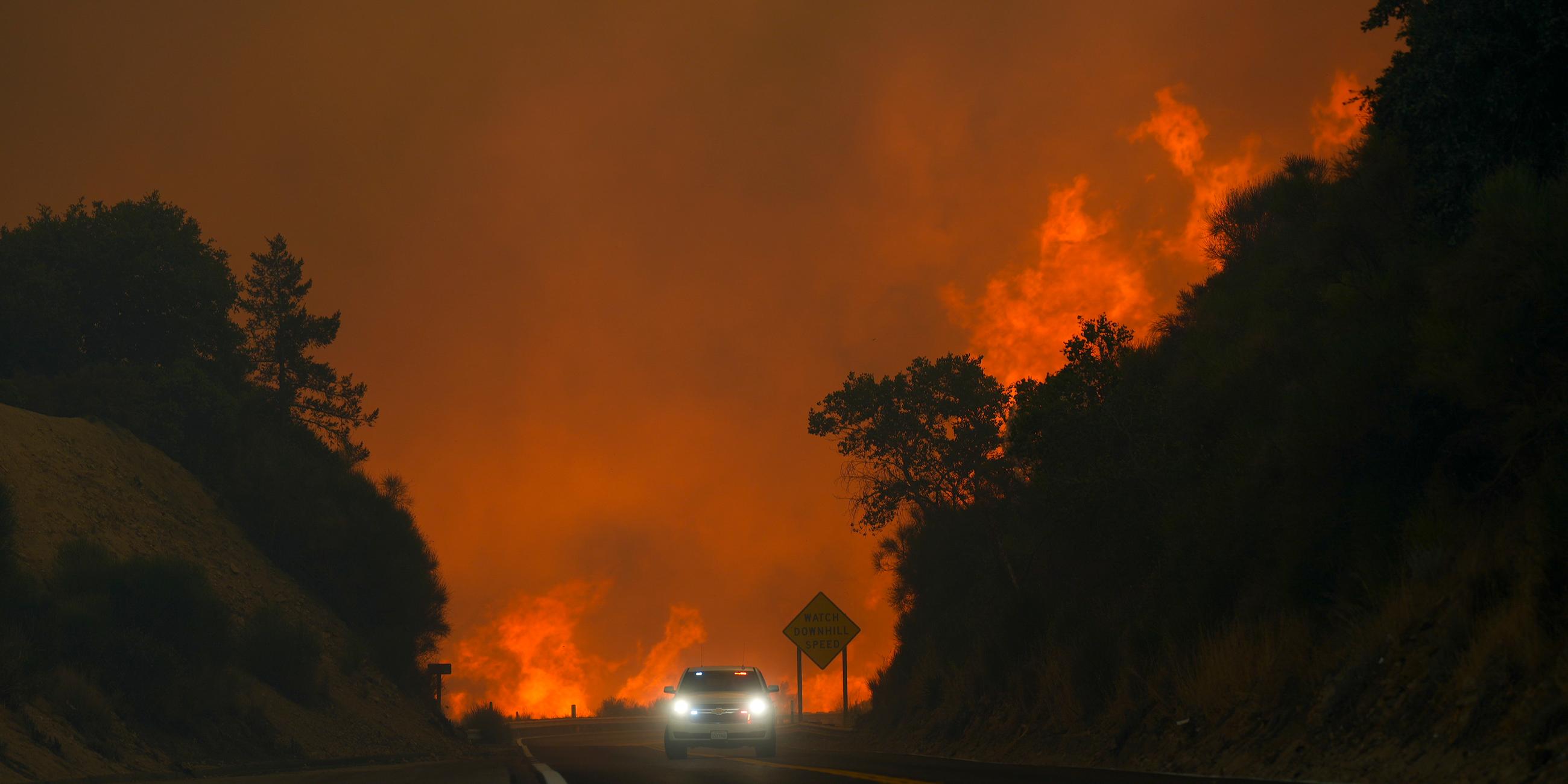 07.09.2024, USA, Running Springs: Das Line Fire überspringt den Highway 330, als ein Autofahrer in der Nähe von Running Springs vorbeifährt.