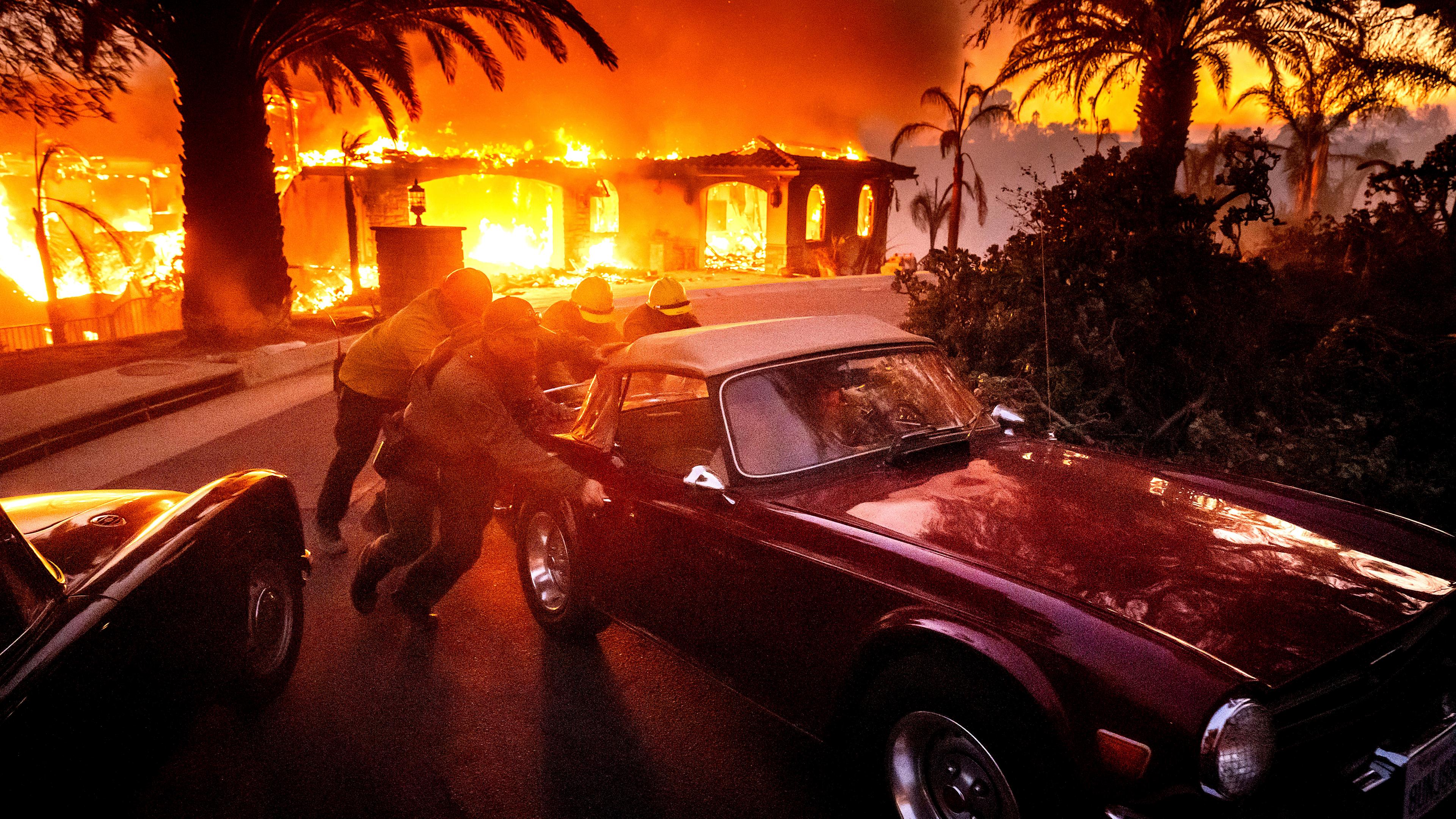 Feuerwehrleute und Sheriffs schieben einen Oldtimer von einem brennenden Haus weg, während das "Mountain Fire" brennt. 