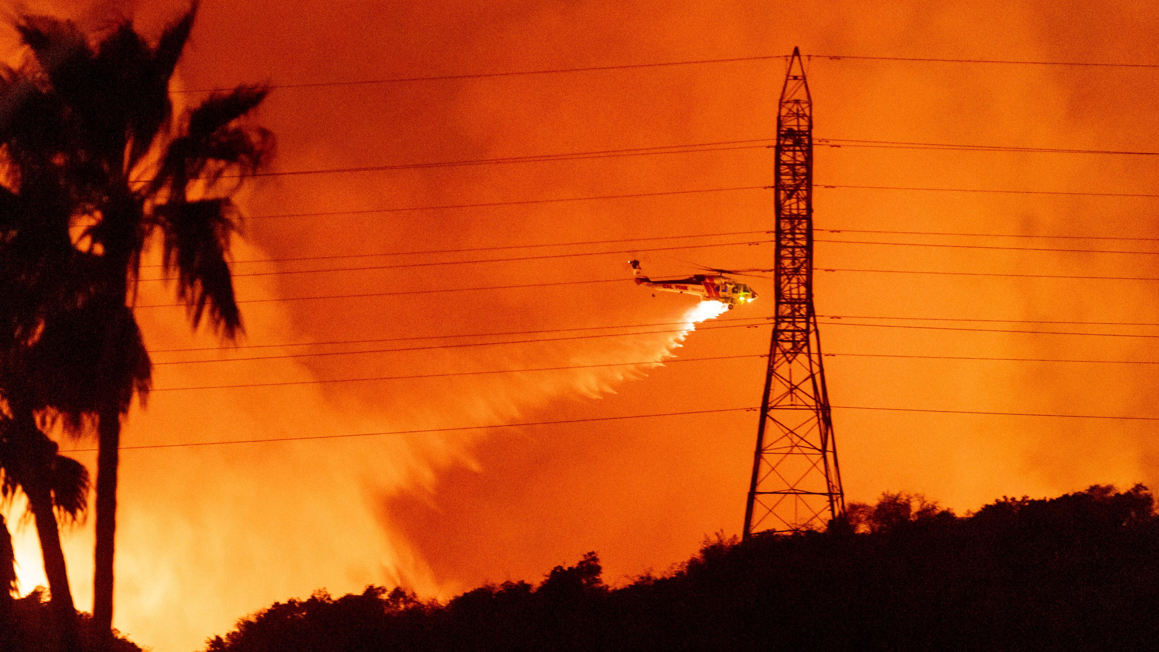 Ein Helikopter fliegt über einen Waldbrand und verteilt Löschwasser