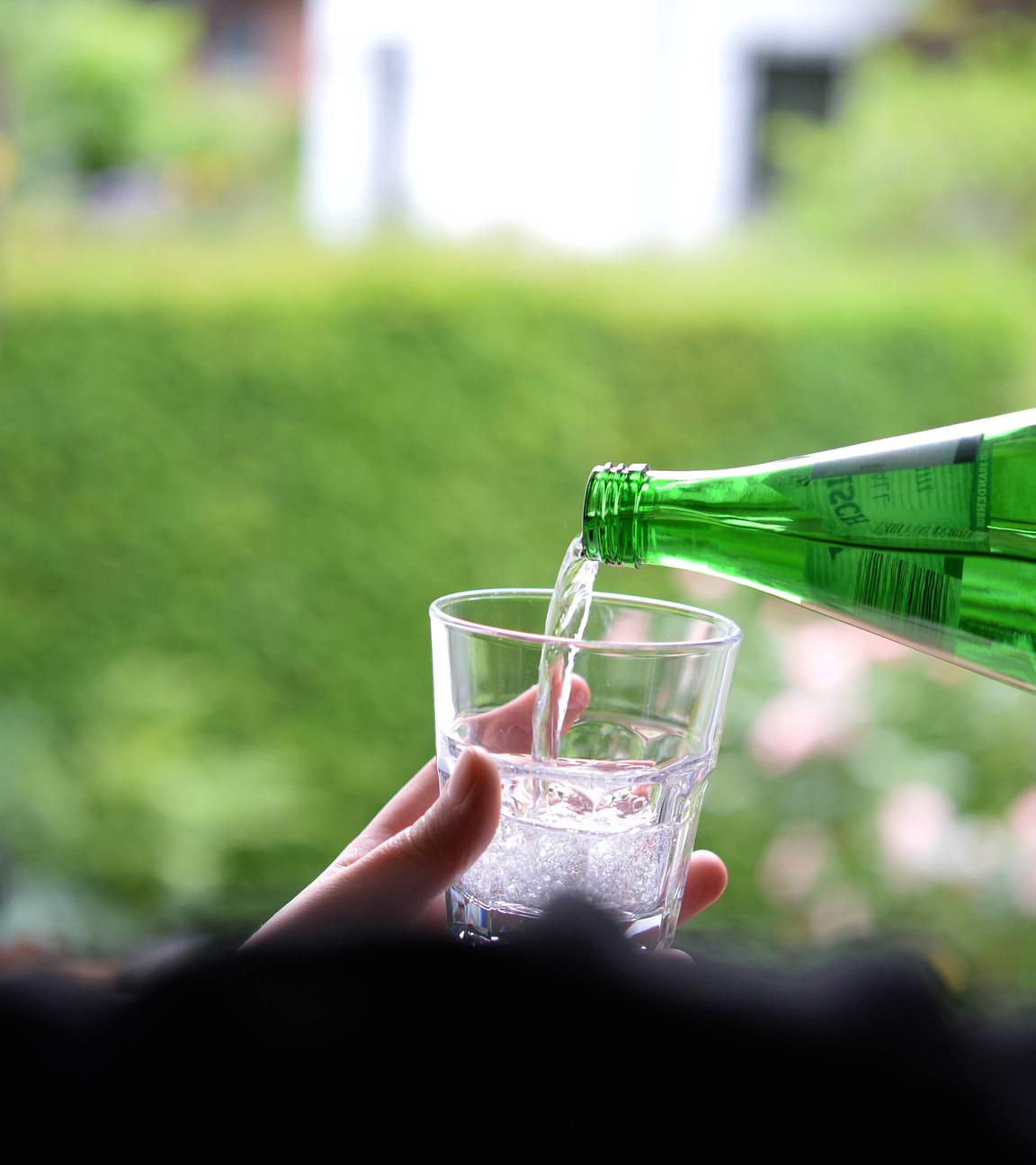 Wasser wird aus Flasche in Glas eingeschenkt.