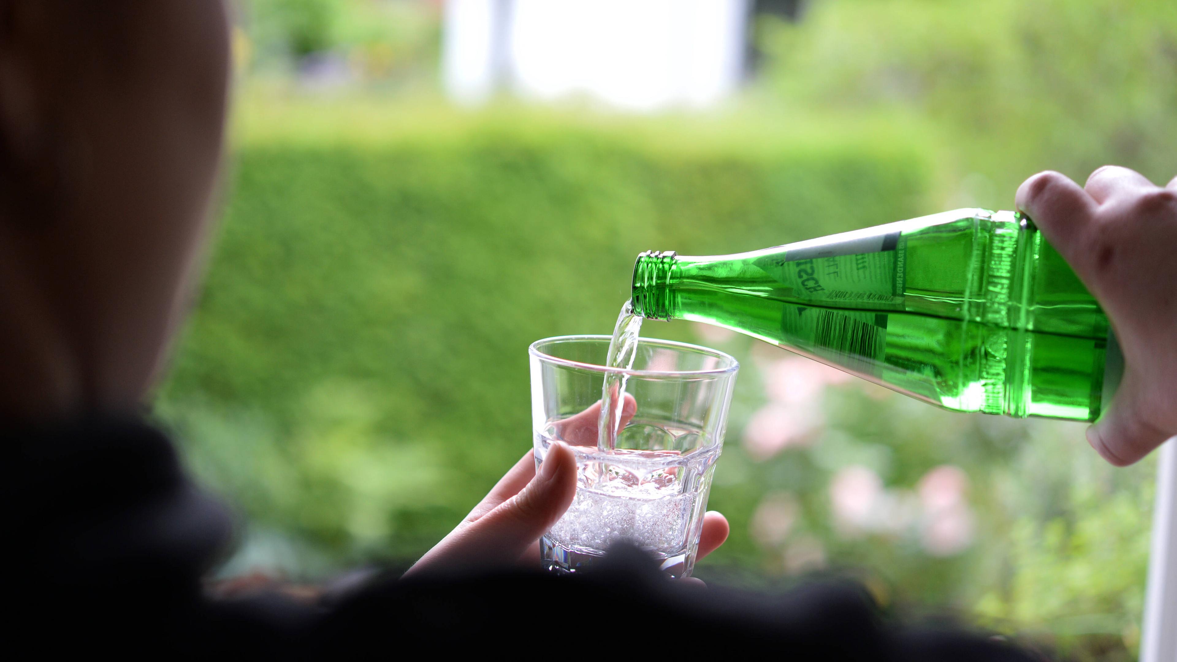 Wasser wird aus Flasche in Glas eingeschenkt.