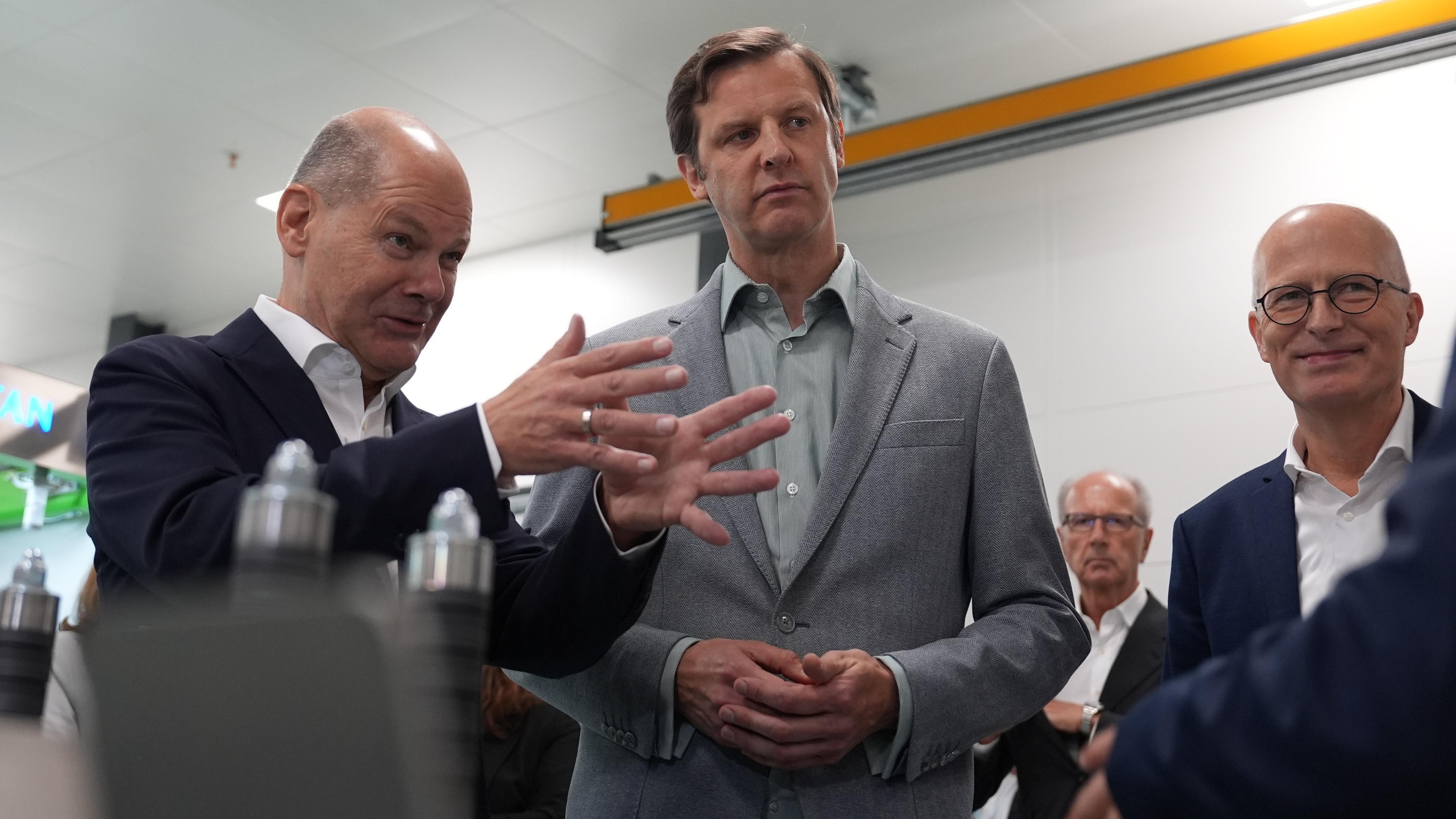 Hamburg: Bundeskanzler Olaf Scholz (l, SPD) steht mit Robin von Plettenberg (M), Sprecher des Vorstands von Quest One GmbH, sowie Peter Tschentscher (r, SPD), Erster Bürgermeister von Hamburg, in der Stack-Fertigungslinie «Titan» vor der Eröffnung des Gigahubs für grüne Wasserstofftechnologie von Quest One. 