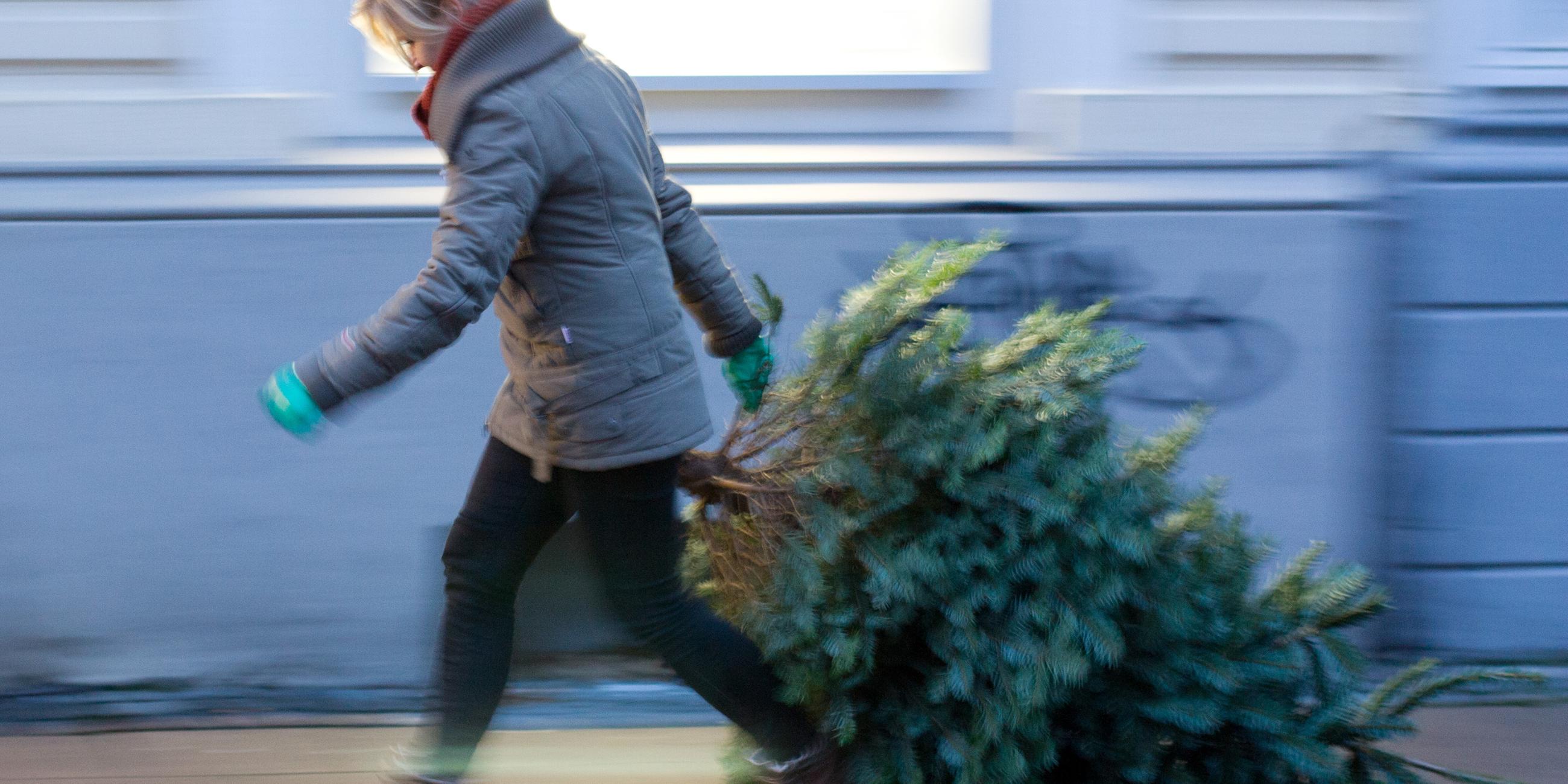 Frau bringt Weihnachtsbaum auf die Straße.