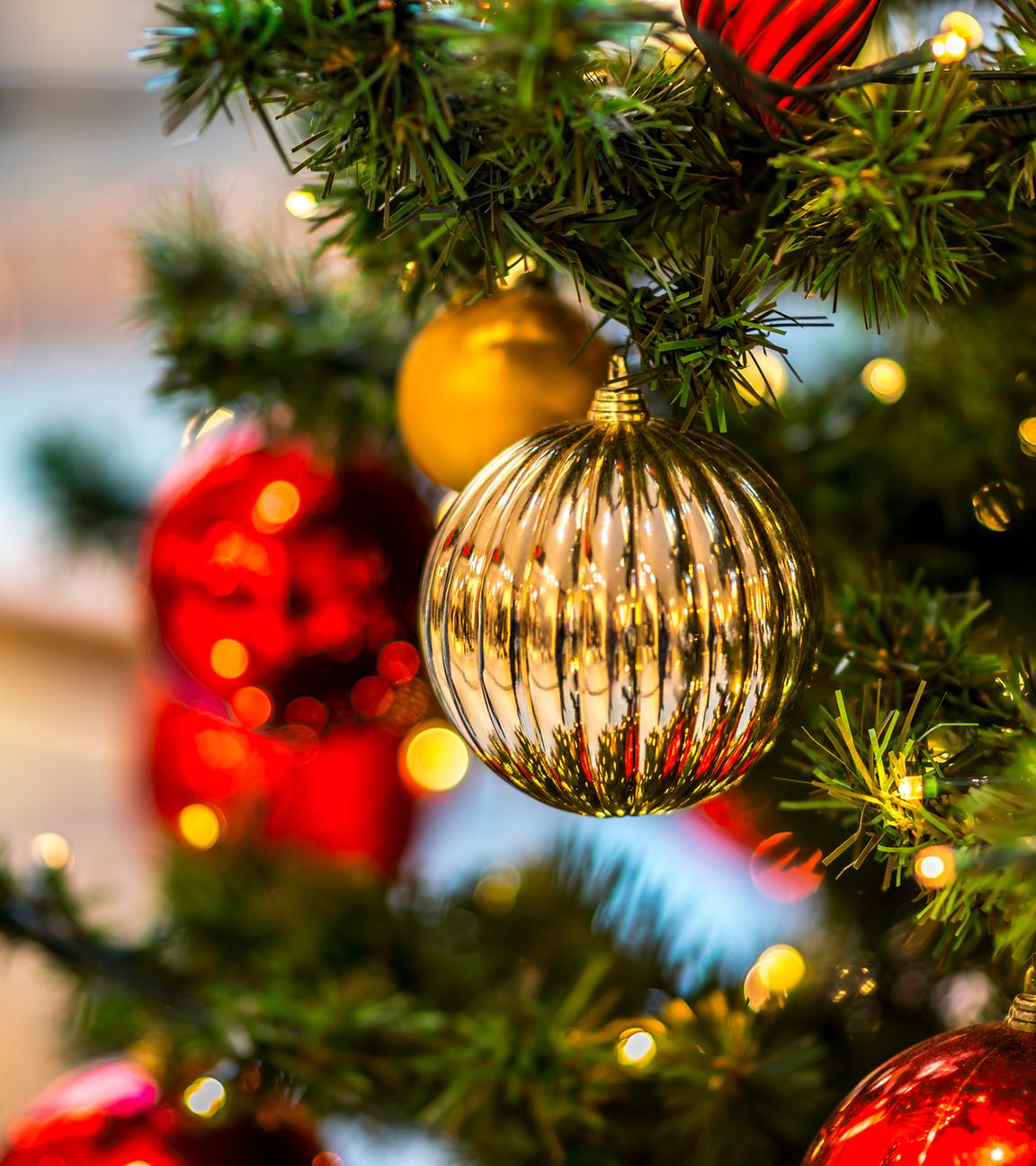 Eine goldene Weihnachtskugel hängt an einem geschmückten Christbaum.