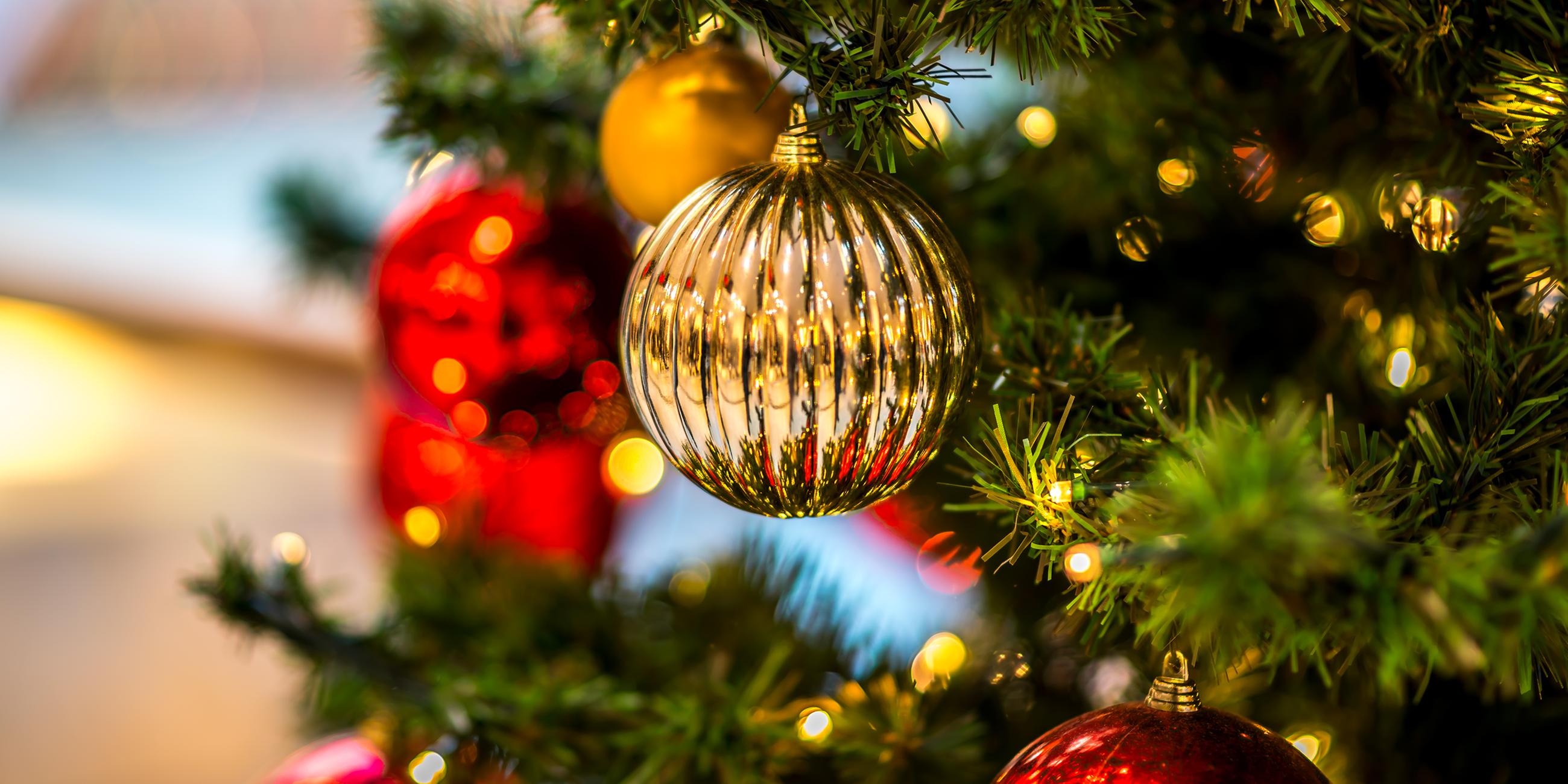 Eine goldene Weihnachtskugel hängt an einem geschmückten Christbaum.