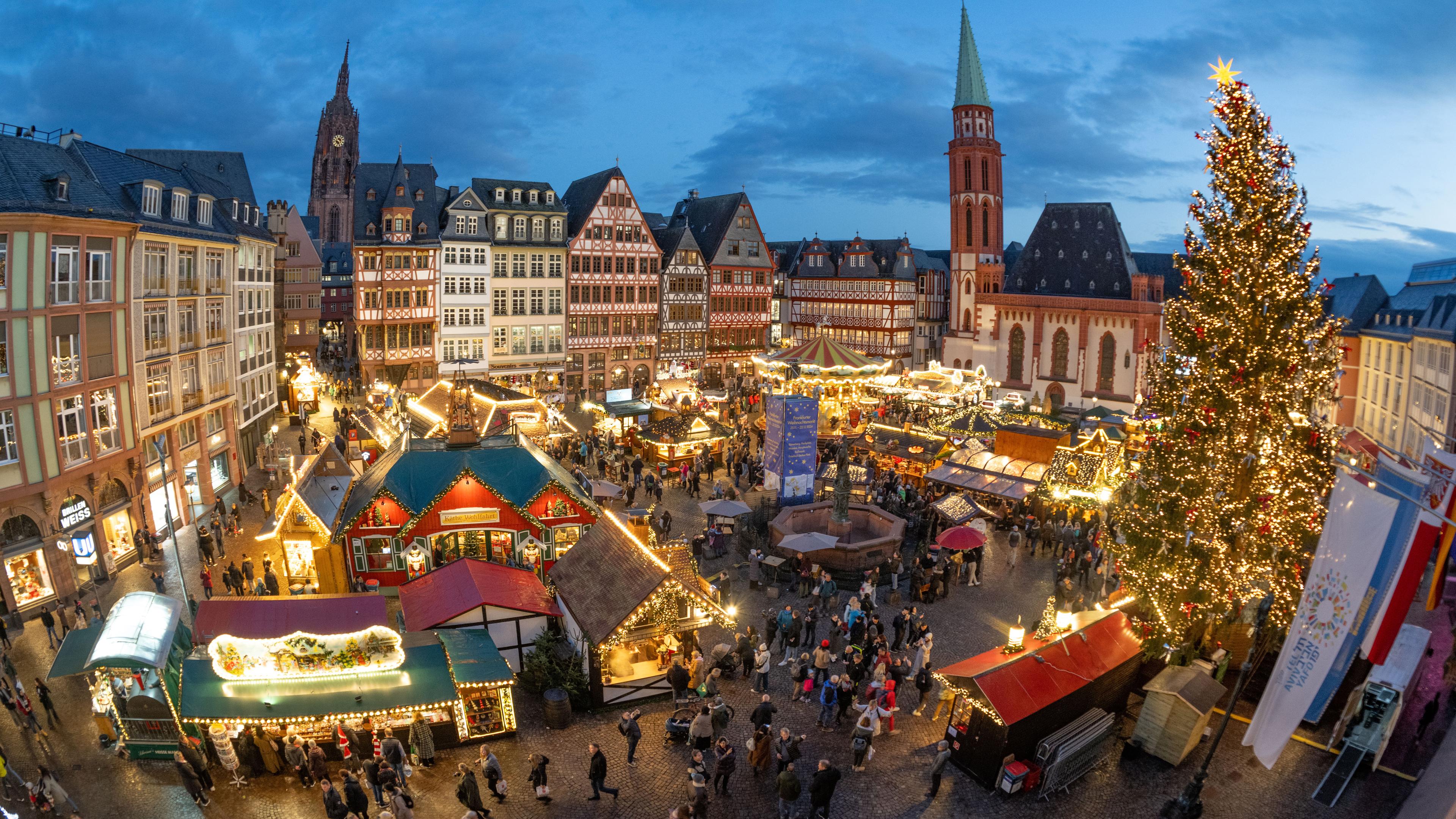 Hessen, Frankfurt/Main: Die Lichter von Verkaufsbuden und Fahrgeschäften leuchten neben dem Weihnachtsbaum "Florian" auf dem traditionellen Weihnachtsmarkt auf dem Römerberg in Frankfurt.