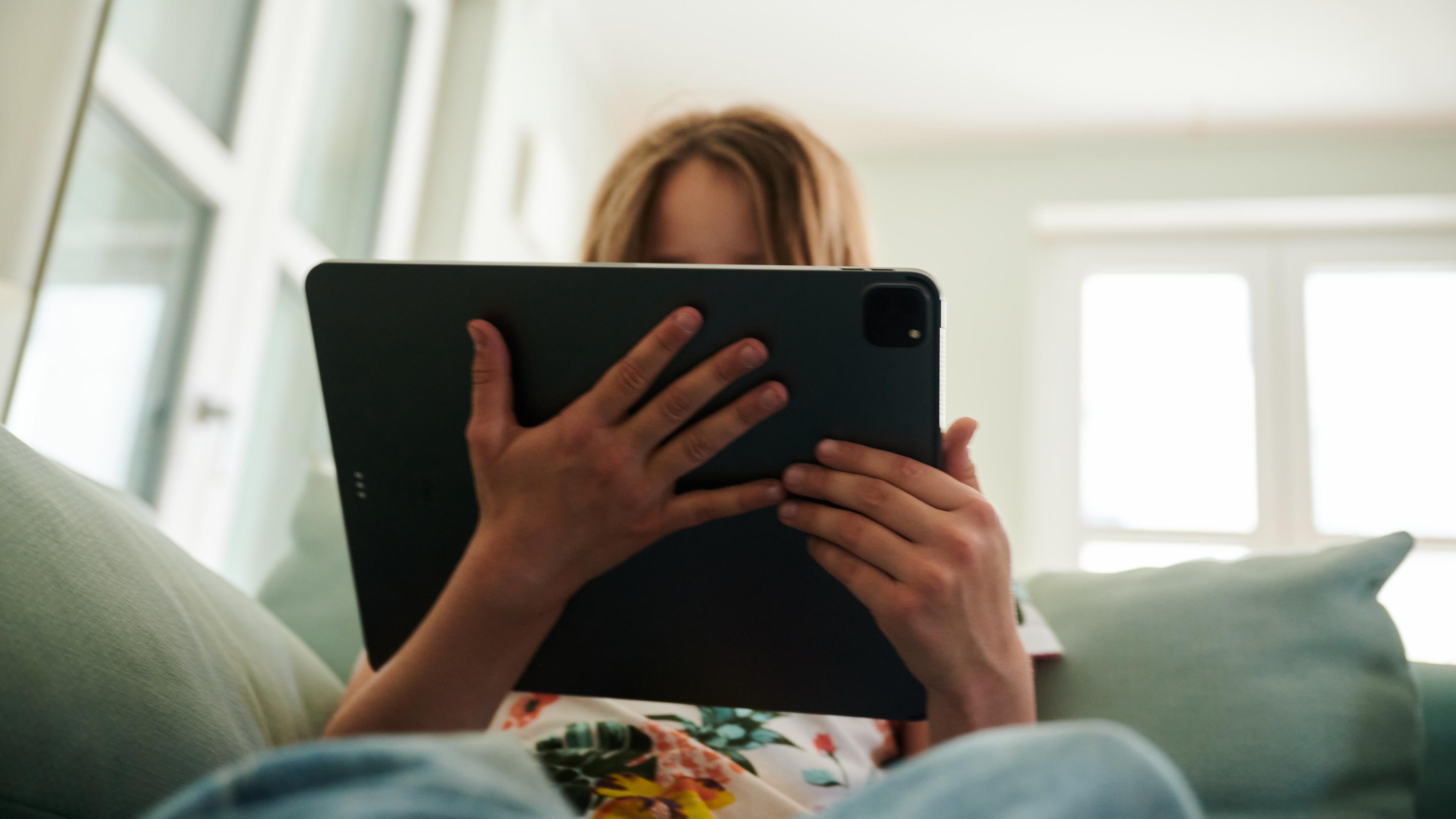 Symbolbild: Ein Mädchen sitzt auf der Couch und guckt auf ein Tablet