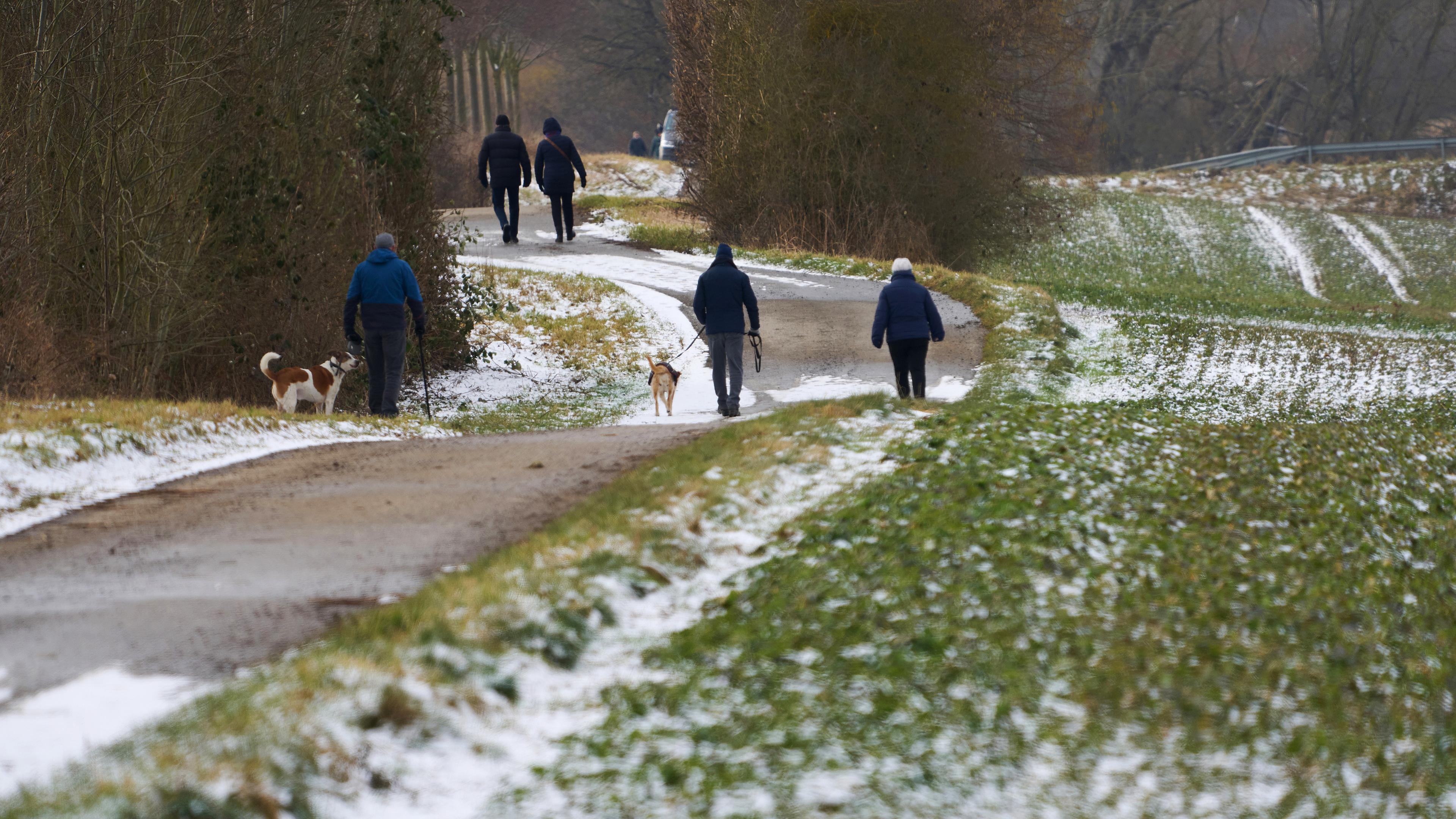 Spaziergänger gehen am Rand der Felder entlang, auf denen der Schnee langsam taut, aufgenommen am 16.02.2025 in Mayen (Eifel)