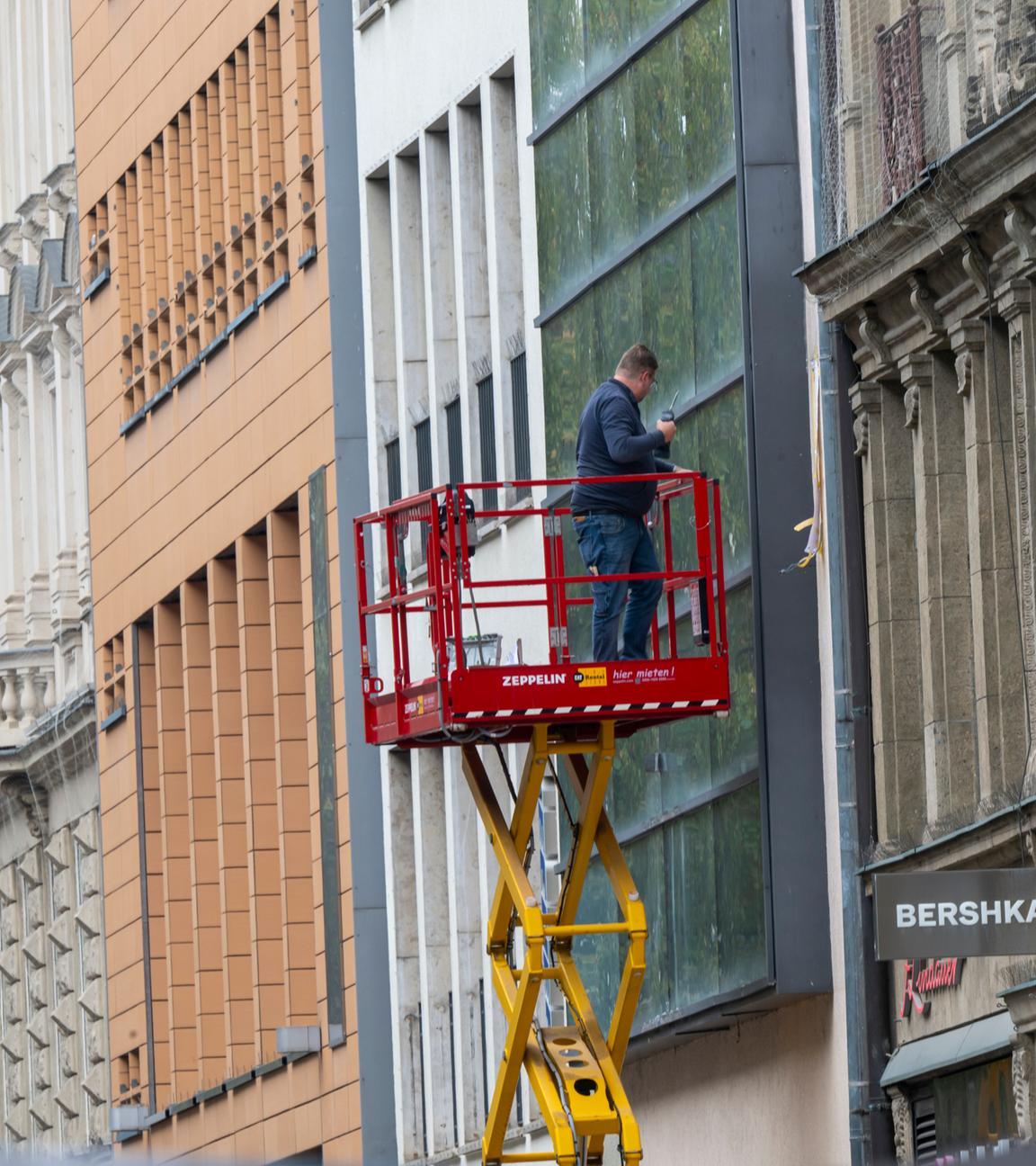 Ein Mann auf einer Hebebühne bearbeitet in einer Fußgängerzone eine Fassade