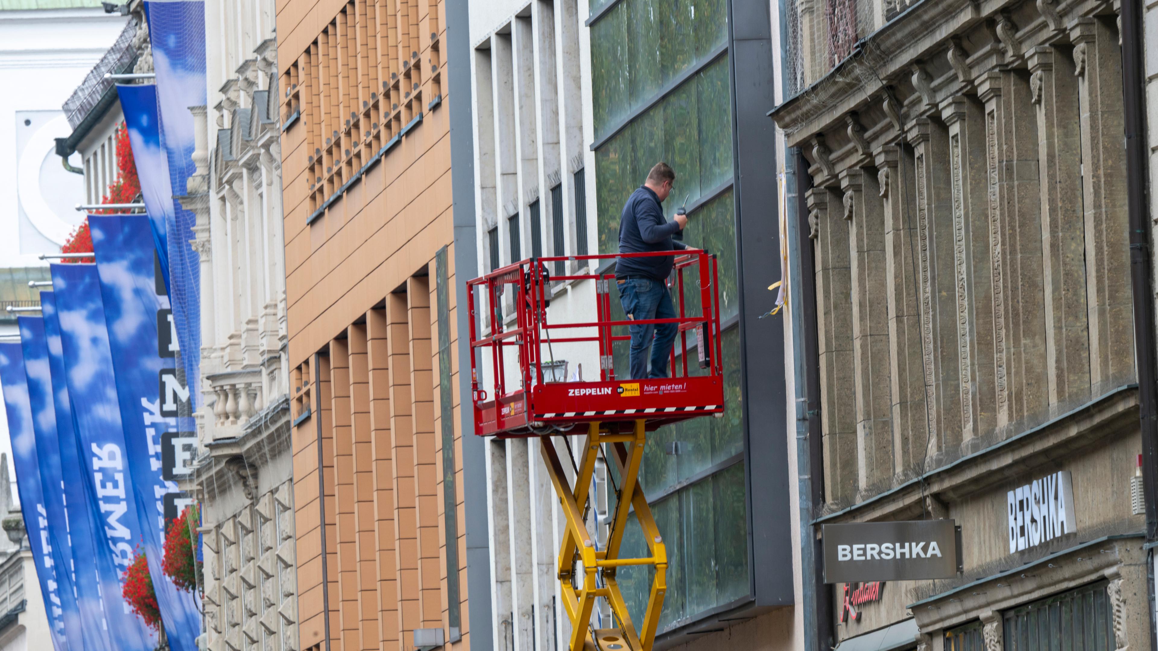 Ein Mann auf einer Hebebühne bearbeitet in einer Fußgängerzone eine Fassade