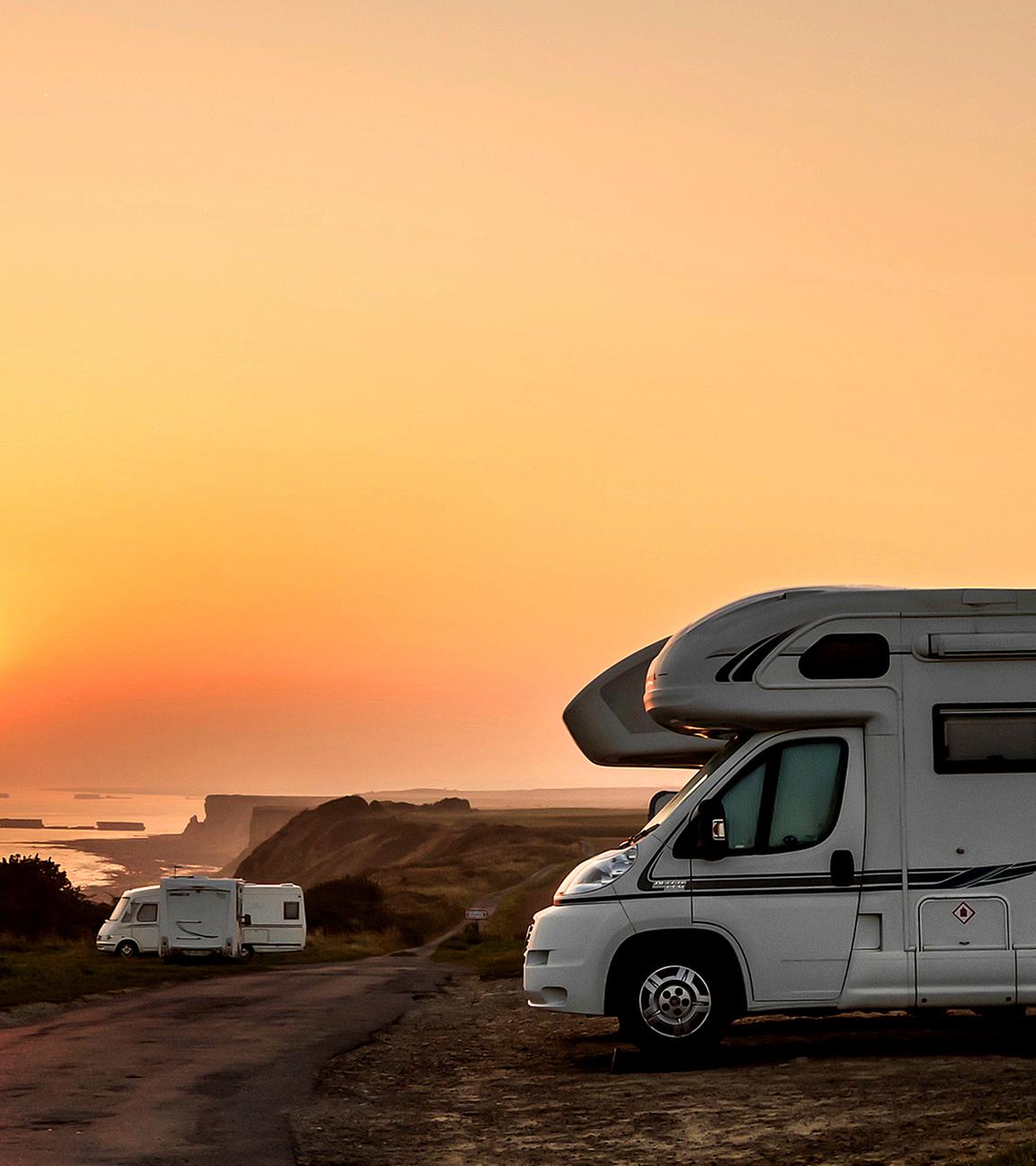 Wohnmobil an Küstenlandschaft vor untergehender Sonne.