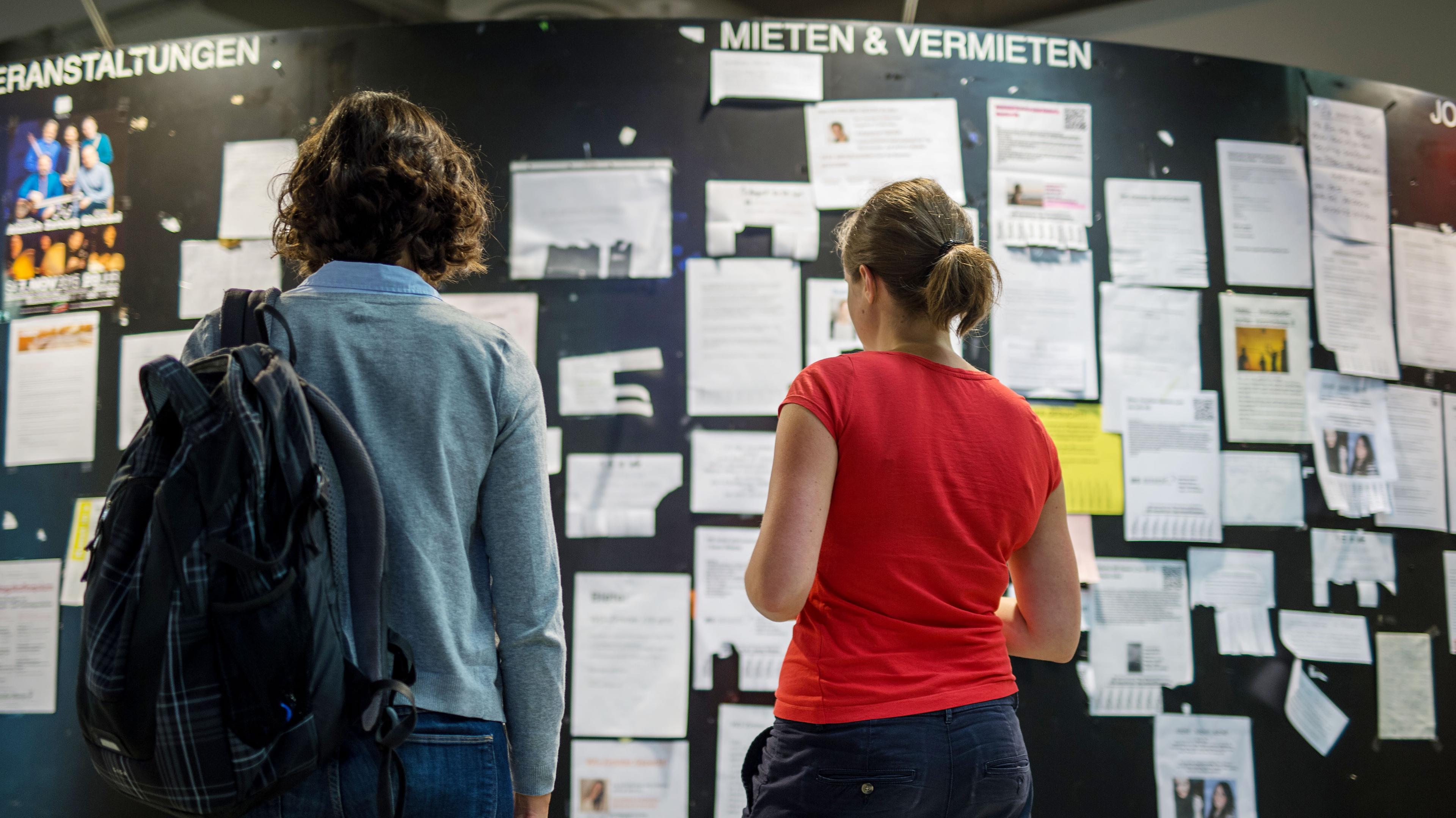 Zwei Studentinnen betrachten die Wohnungsanzeigen am Schwarzen Brett in der Mensa der Ludwig-Maximilians-Universität