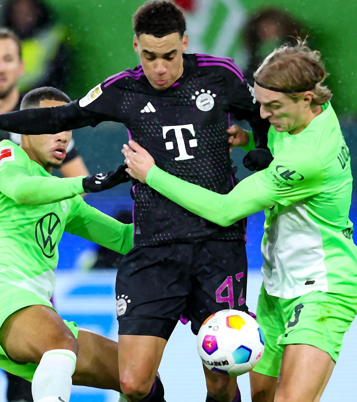 Bayern Münchens deutscher Mittelfeldspieler #42 Jamal Musiala (C), Wolfsburgs belgischer Verteidiger #03 Sebastiaan Bornauw (R) und Wolfsburgs belgischer Mittelfeldspieler #06 Aster Vranckx (L) kämpfen um den Ball.
