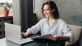 Woman sits in her home and uses a laptop.