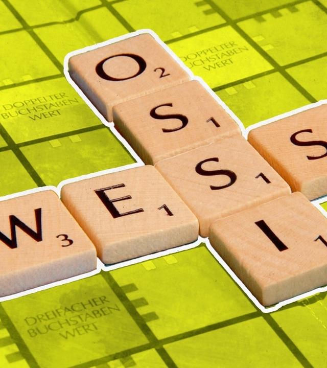 Ein Scrabble-Brett mit den Worten „Ossi” und „Wessi”, die sich in der Mitte überschneiden. Das Wort Ossi gibt 5 Punkte und das Wort Wessi ergibt 7 Punkte.