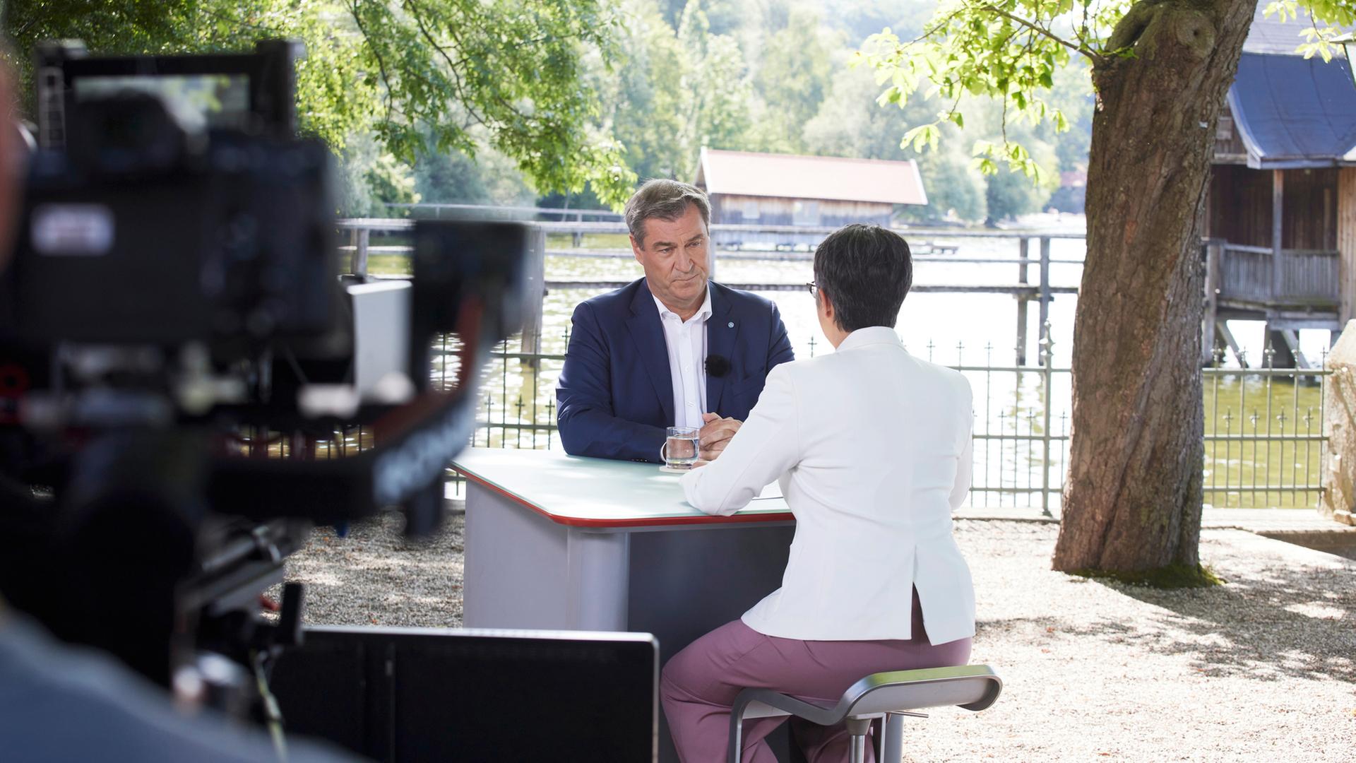"Berlin direkt - Sommerinterview": Markus Söder und Shakuntala Banerjee sitzen sich zum Gespräch an einem Tisch gegenüber.