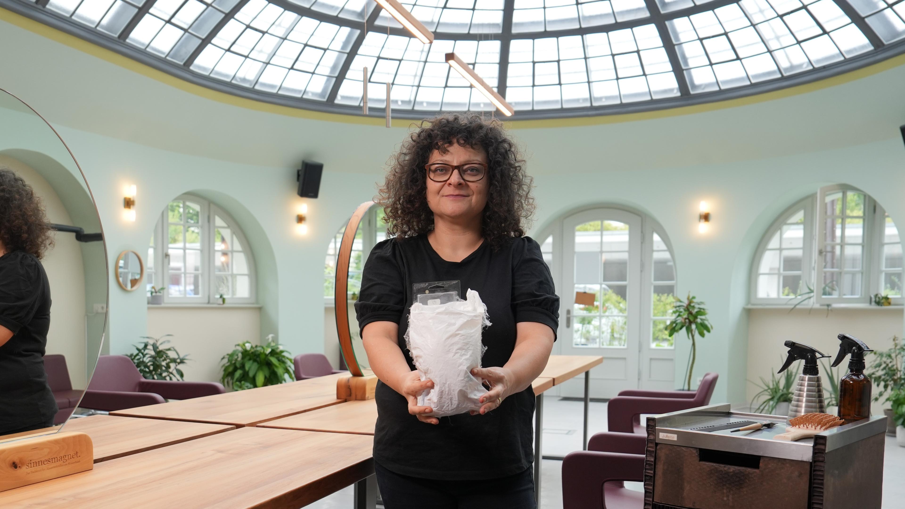 Die Friseurmeisterin und Gründerin des ersten Zero-Waste-Friseursalons Juliette Beke lächelt in die Kamera mit einem Liter Abfall in der Hand.