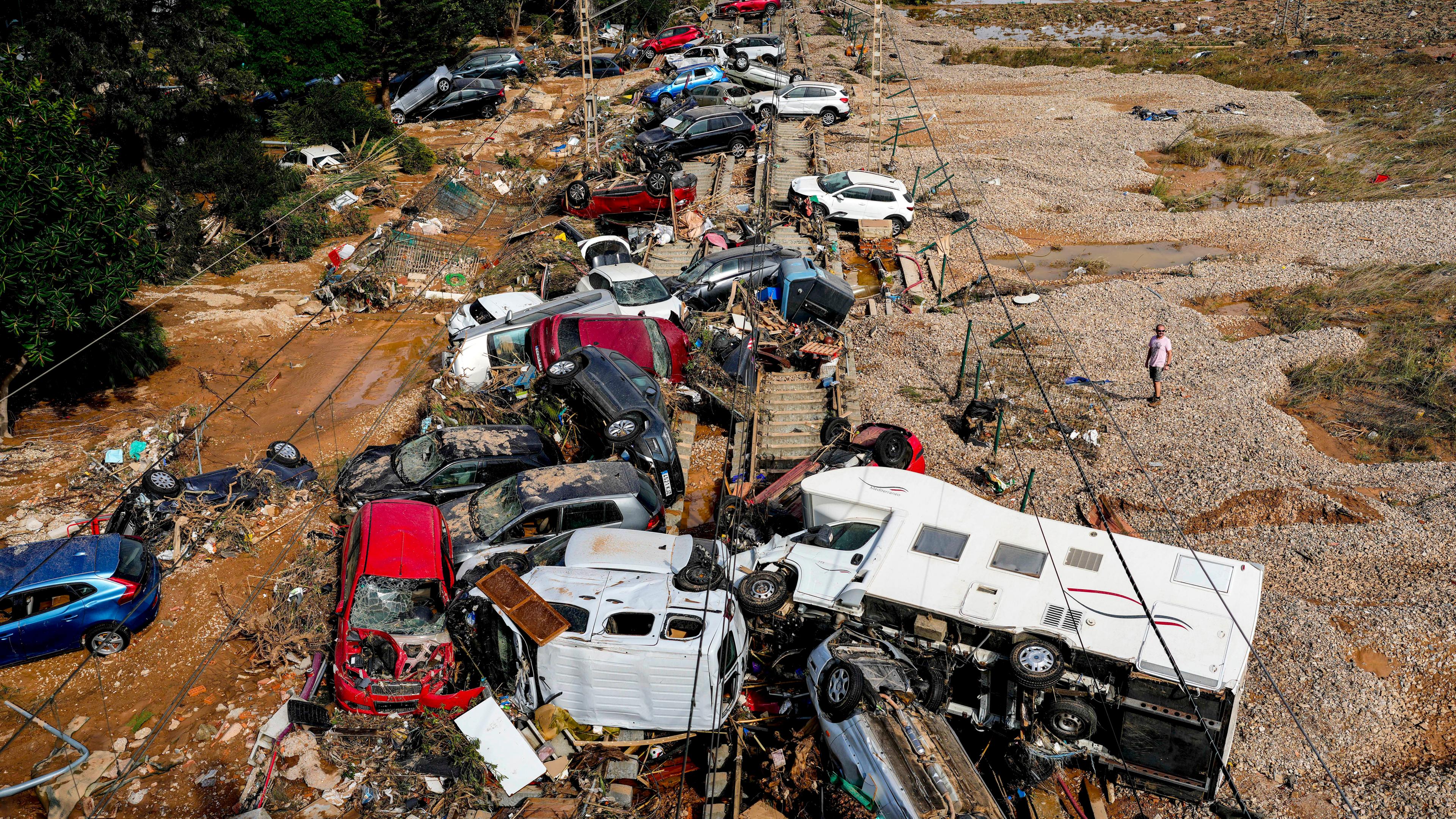 Ein Mann steht neben Autos, die nach dem Unwetter übereinander liegen. 