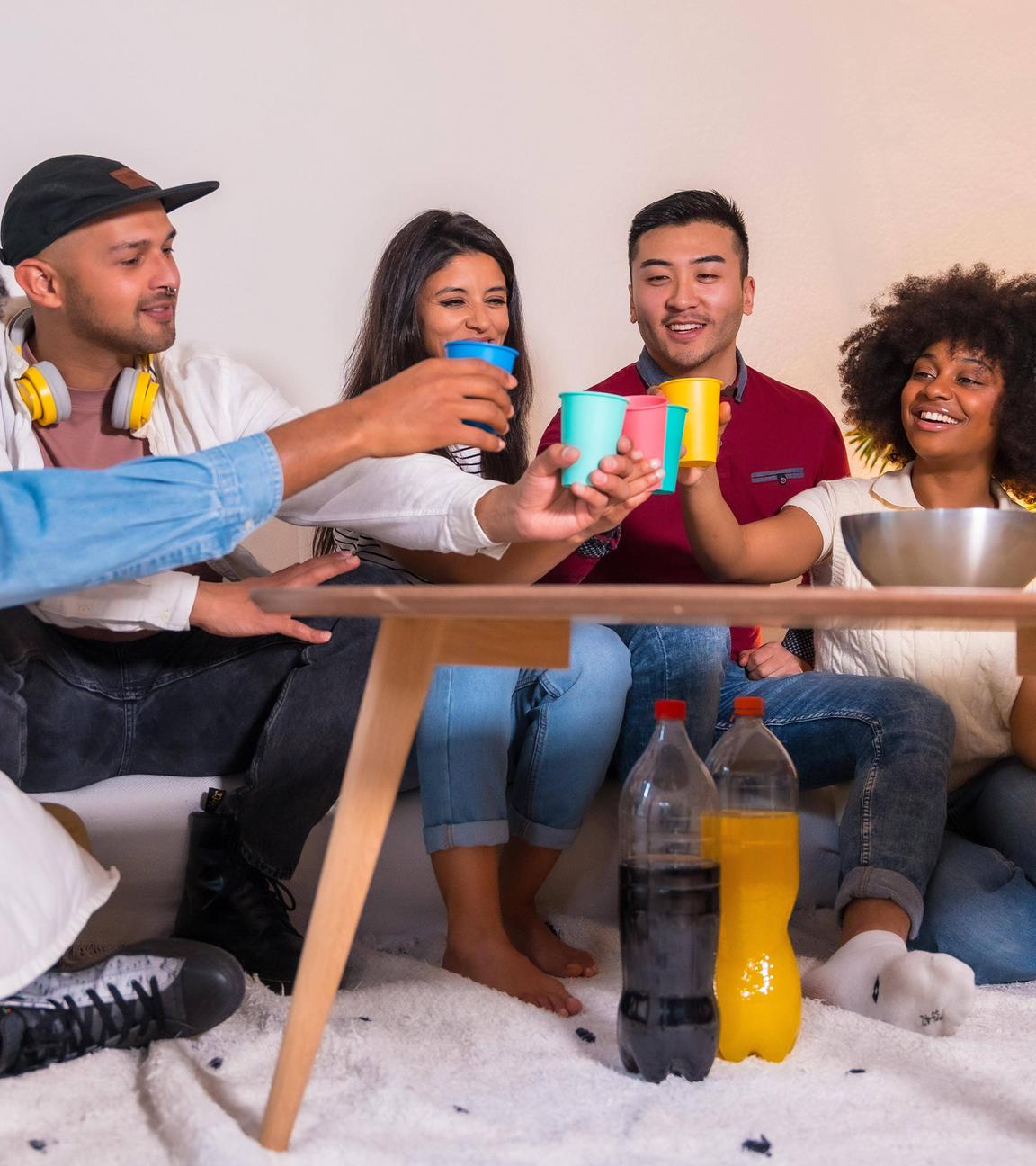 Eine Gruppe von Freunden isst Popcorn und stößt mit Softdrinks an (Symbolfoto)