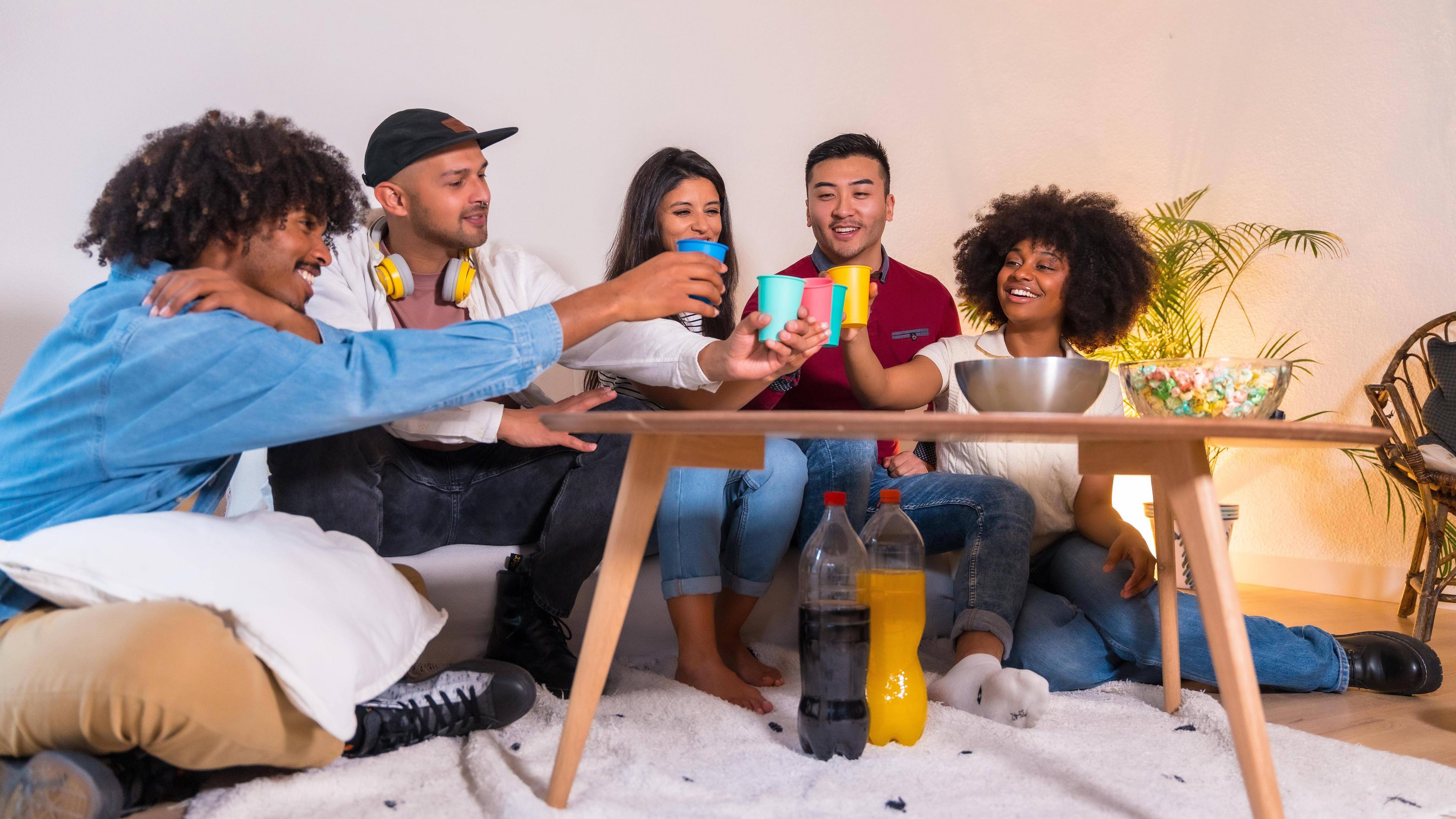 Eine Gruppe von Freunden isst Popcorn und stößt mit Softdrinks an (Symbolfoto)